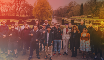 A group of smiling people stood outside in some gardens, with an orange tinted overlay.